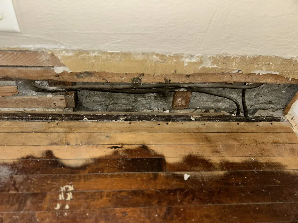 Floor edge opened at the wall showing old wiring below